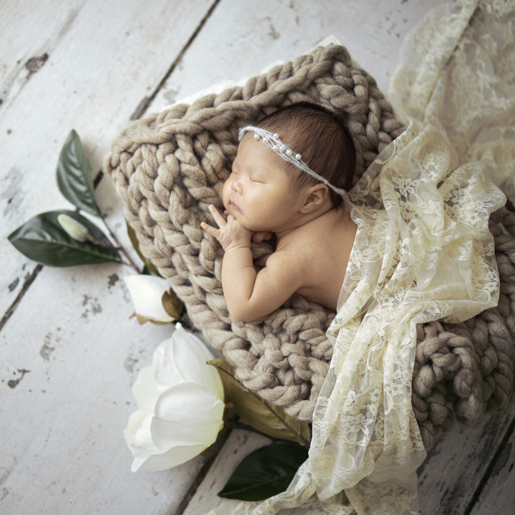 newborn baby girl on woven blanket with magnolia flowers and lace