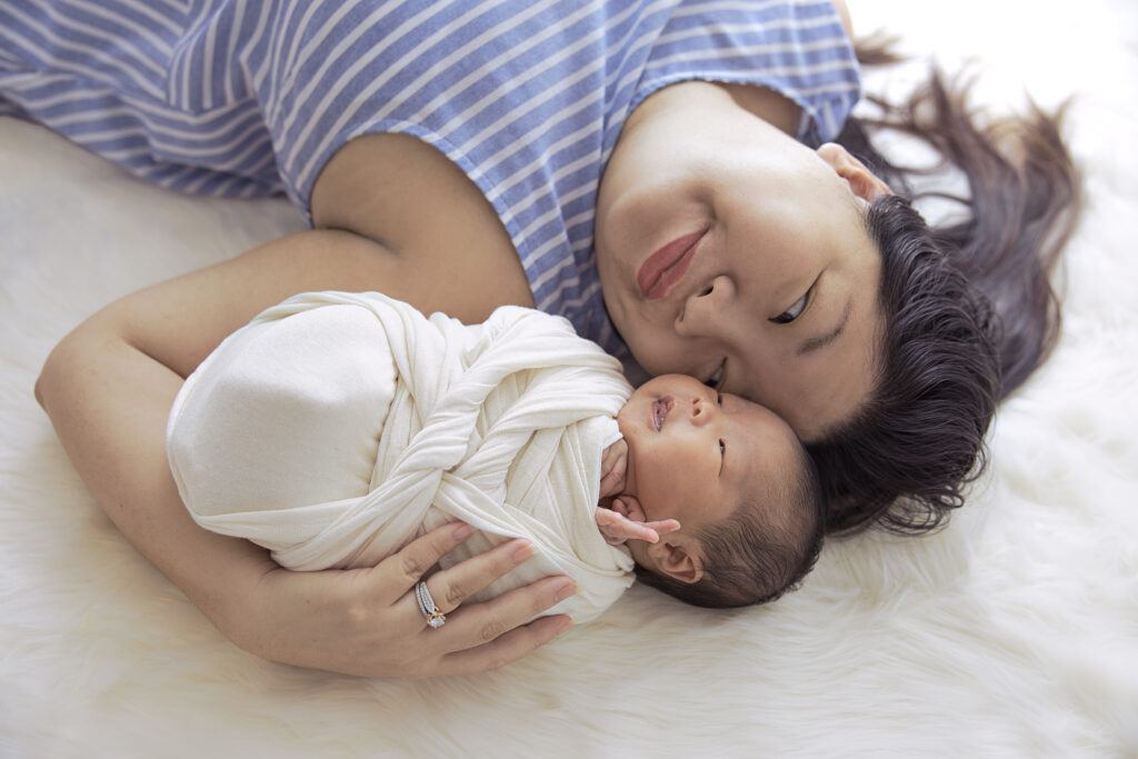 professional newborn photography of a mom and baby laying with their heads together
