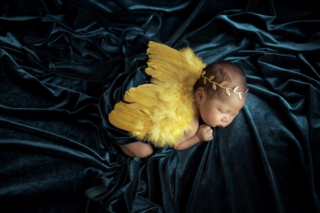 newborn baby girl on teal blue velvet with golden angel wings