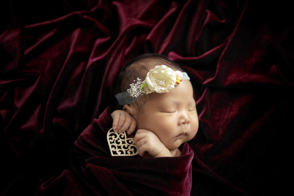 newborn baby on red velvet holding wooden heart