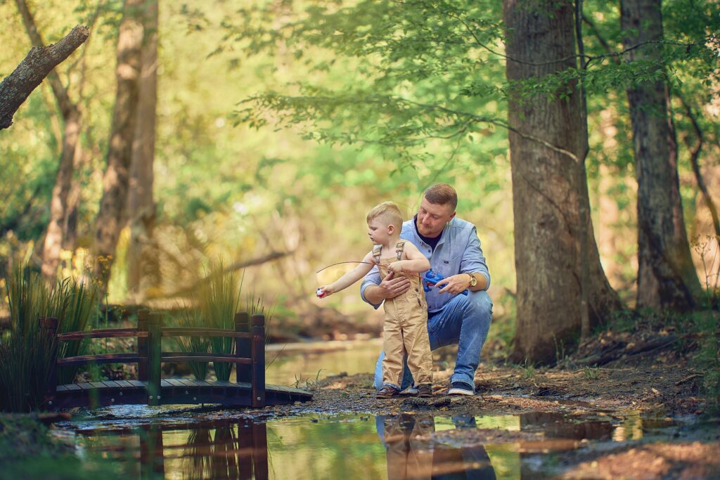 father helping son with a fishing rod on the bank of a woodland stream