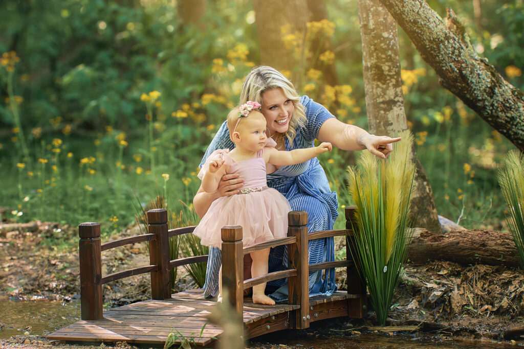 mother and toddler daughter standing on bridge point into distance