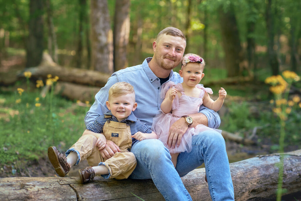 dad and children sitting on log surrounded by wild flowers, shot in our gwinnett county scenic studio location