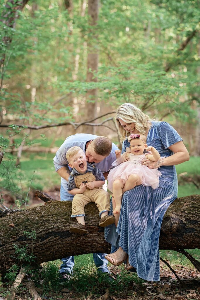 mom and dad tickling young children on a mossy log in the woods