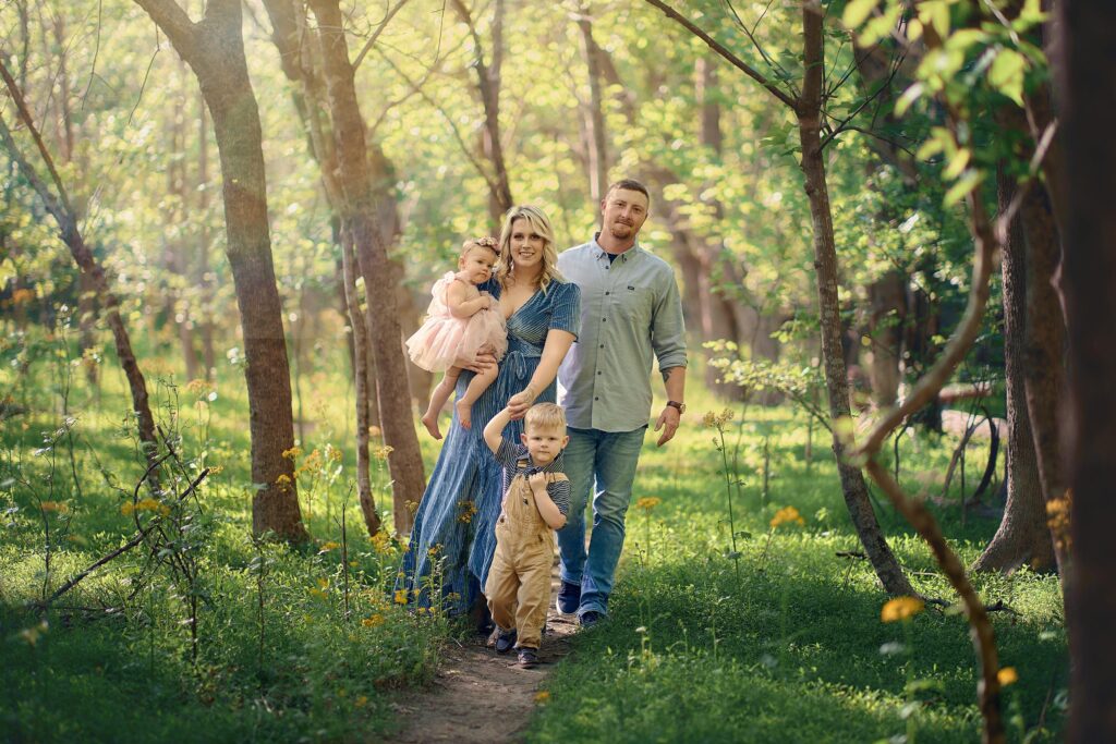 natural scenic photo of mom dad and children walking through meadow with trees and vines surrounding them