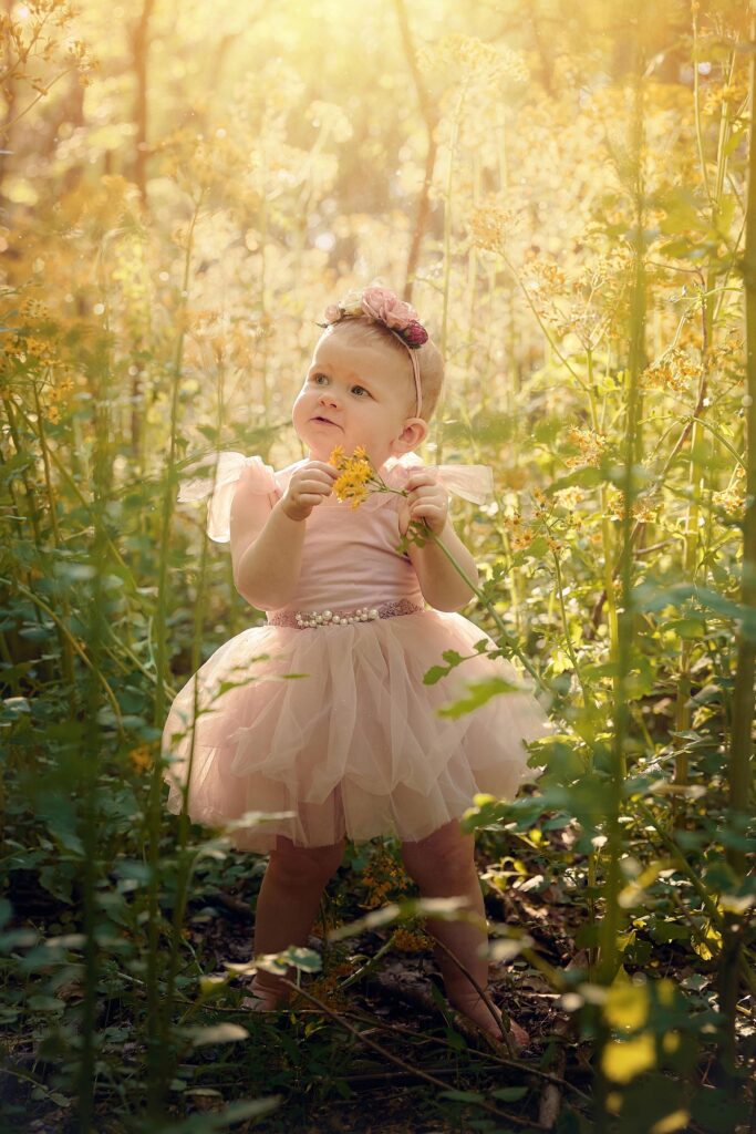 toddler girl in pink tutu in a field of golden wild flowers in a natural park